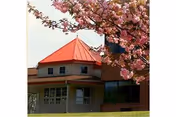 Front view of a brick senior living facility with a red roof and pink blossoms.