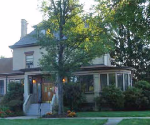 Two-story senior living facility with a front entrance and surrounding trees.
