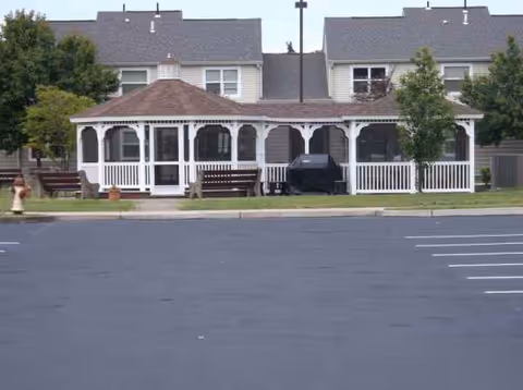 Front view of Rosewood Apartments with a white porch, benches, and surrounding trees.