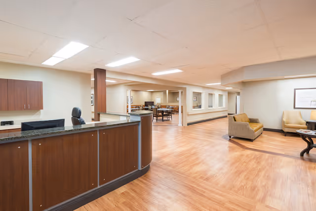 Reception and common area with a curved wood front desk, wood-look flooring, seating, and dining tables.