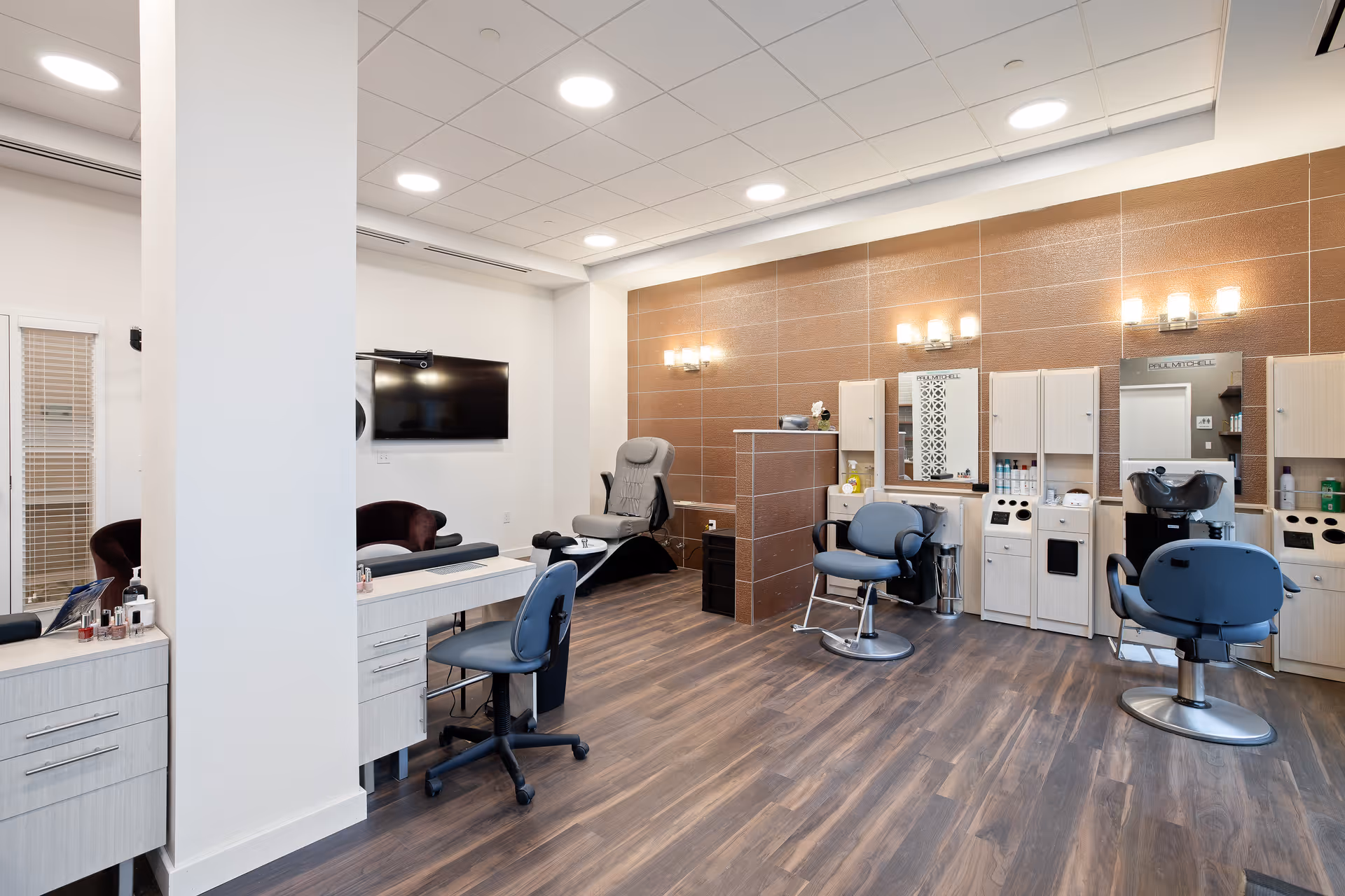 Interior salon with styling chairs, mirrors, manicure stations and a wall-mounted TV.
