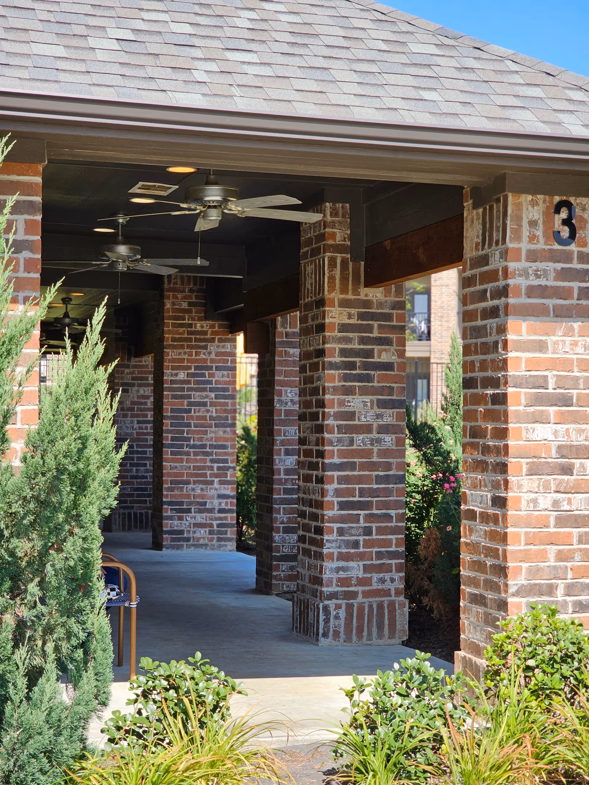 Covered brick colonnade with ceiling fans and landscaping at the exterior of the facility.