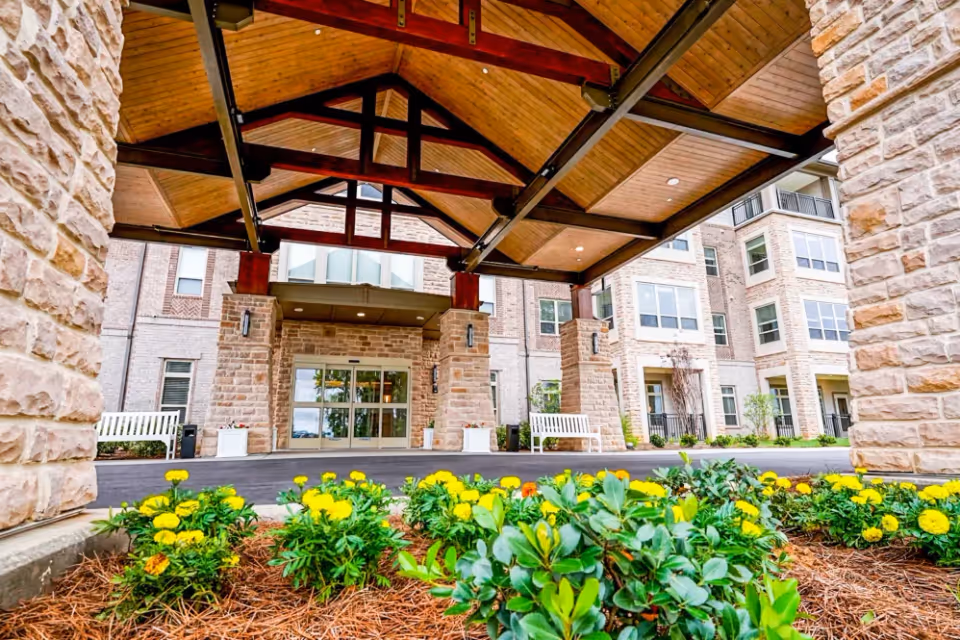 Exterior view of the entrance to Harmony At Mt. Juliet, featuring a wooden canopy supported by stone columns, surrounded by colorful flowers and greenery.