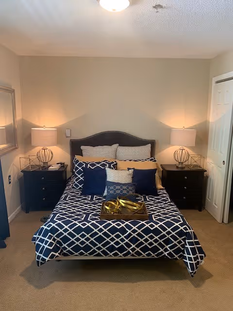 A neatly made bedroom with a navy geometric-pattern bed centered between two nightstands and lamps.