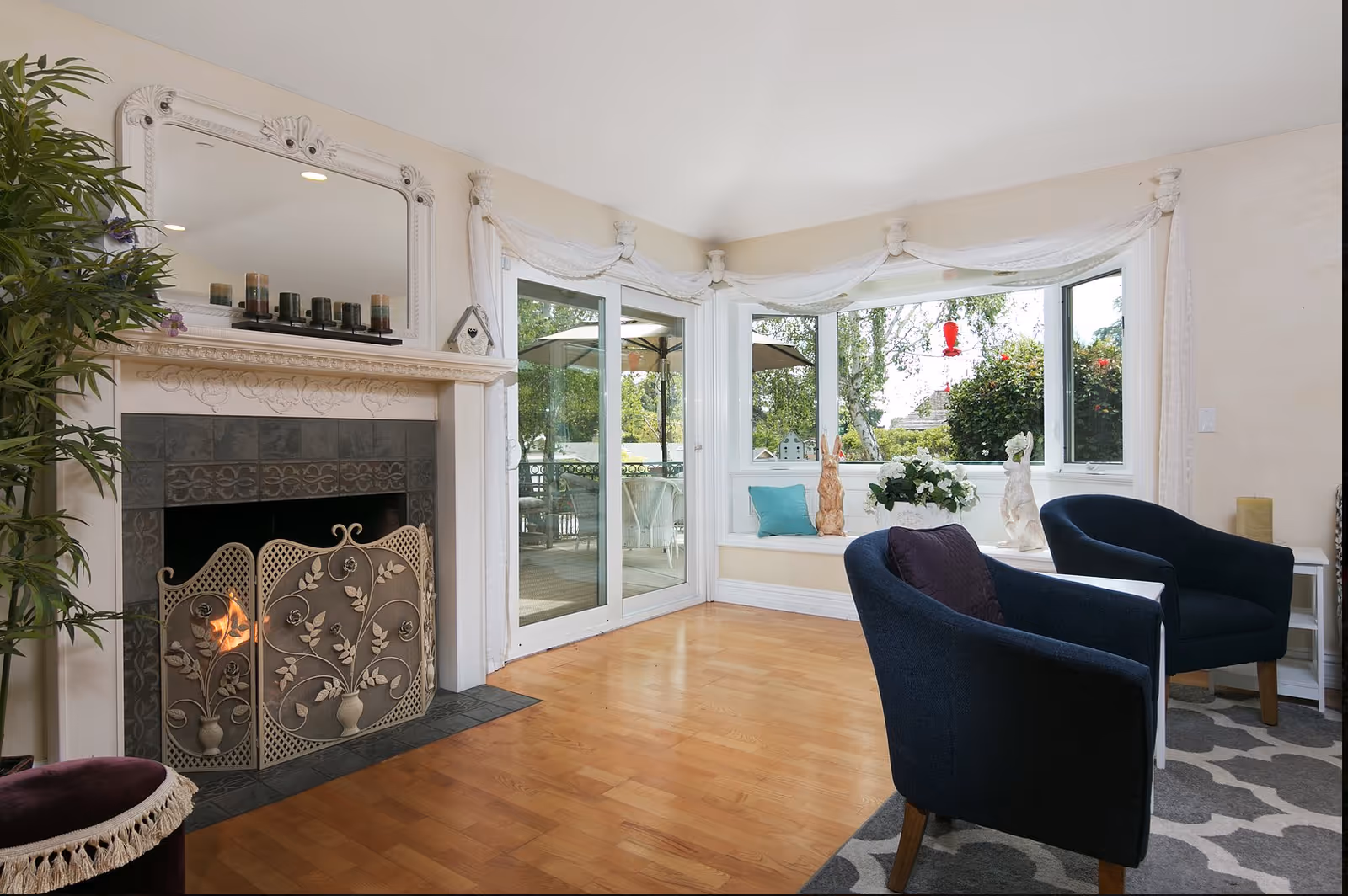 Bright living room with a decorative fireplace, sliding glass door to a patio, bay window seat and two navy armchairs.