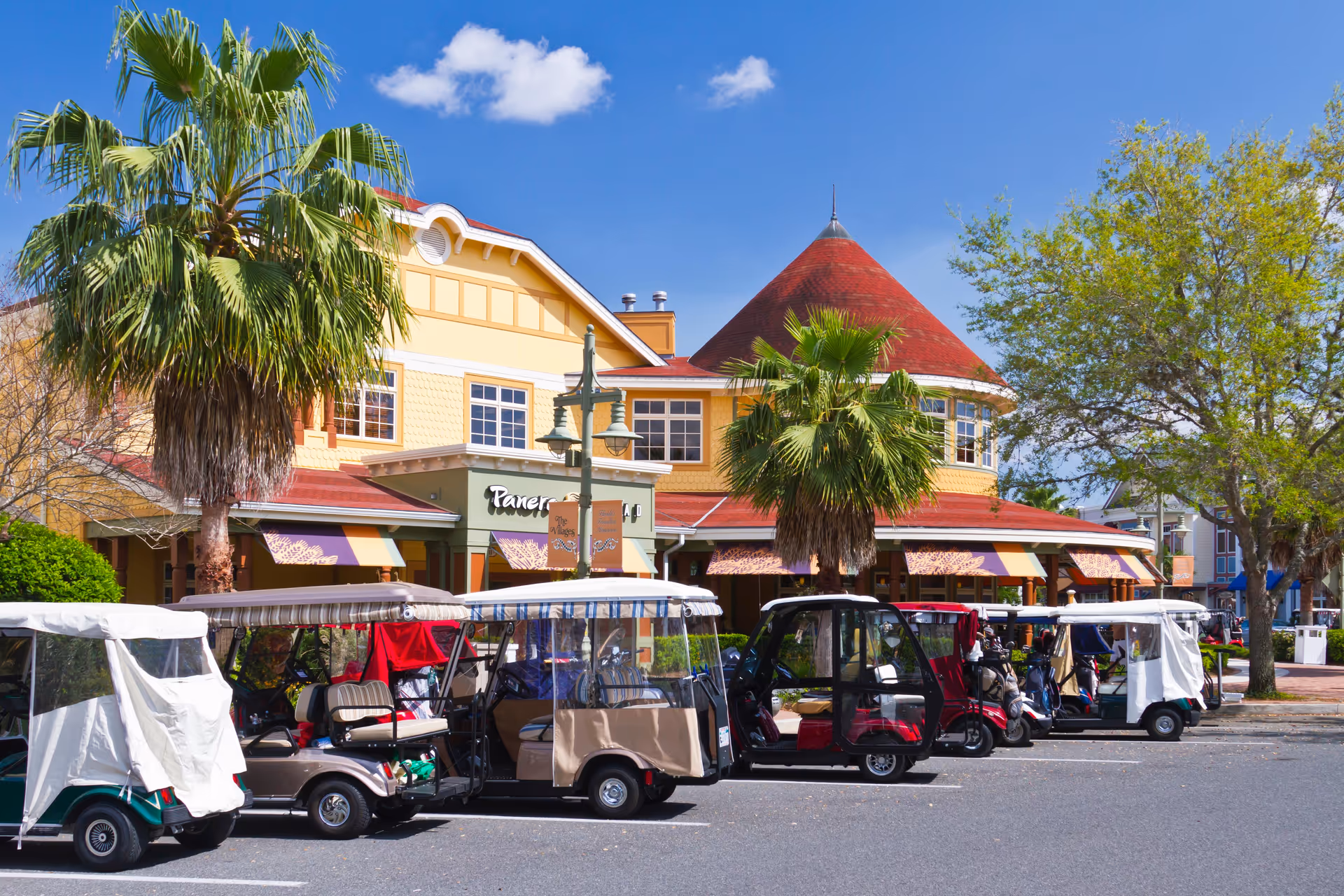 Colorful two-story building with a red turret, palm trees and a row of parked golf carts in front under a blue sky.