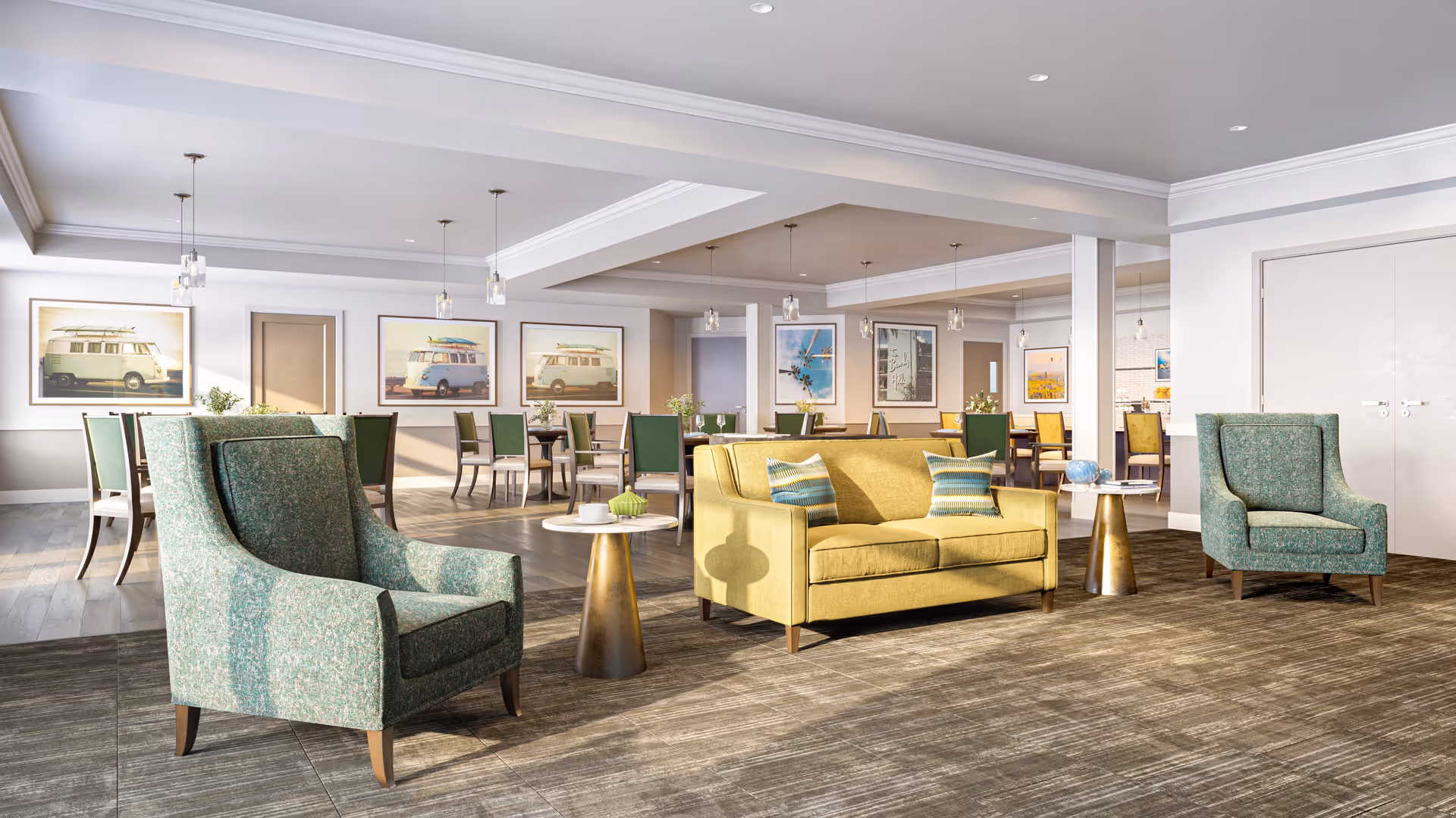A bright and spacious common area with a yellow sofa and two green armchairs arranged around two small round tables. In the background, there are multiple dining tables with green and beige chairs, pendant lights hanging from the ceiling, and framed pictures on the walls featuring vintage vans and scenic views.