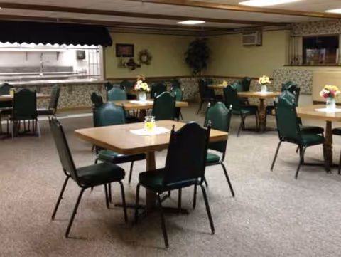 A dining room with several tables, green chairs, and flowers in vases.