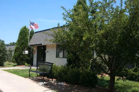 Exterior view of Ridgewood Rehabilitation & Living Center with bench, flag, and trees.