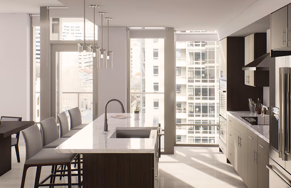 Modern kitchen with a large marble island countertop featuring a sink and faucet, several high chairs along the island, pendant lights hanging above, and large windows letting in natural light with a view of tall buildings outside.