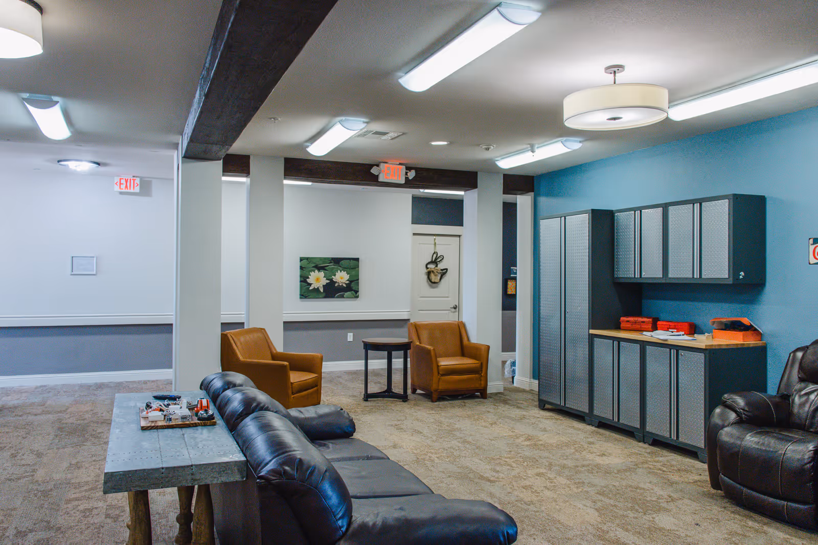 Community lounge with leather sofas and chairs, storage cabinets along a blue wall, and overhead lighting.