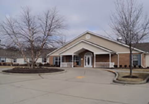 Front exterior of a single-story brick senior living facility with a covered entrance and circular driveway.