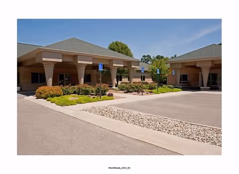 Front entrance of a senior living building with a covered portico, accessible parking signs, and landscaped beds.