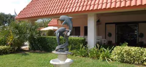 Front exterior of a senior living facility with a dolphin fountain and tropical plants.