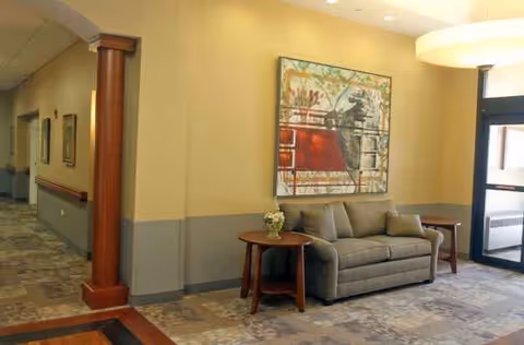 A lounge area with sofa, side table, artwork, and hallway in a facility.