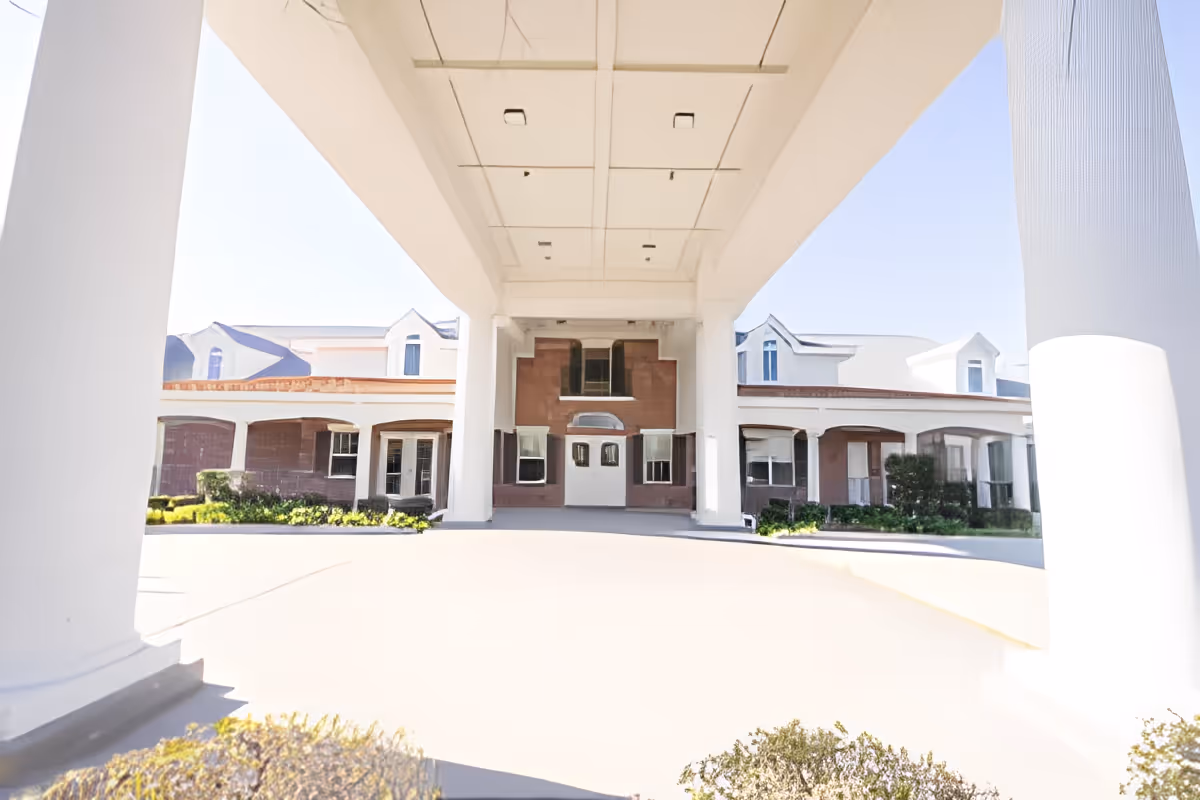 Front entrance under a large porte-cochère with white columns leading to the building facade of a senior living facility.