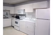 Compact all-white kitchen with cabinets, a sink, microwave over an electric stove, refrigerator, and a front-loading laundry dryer.