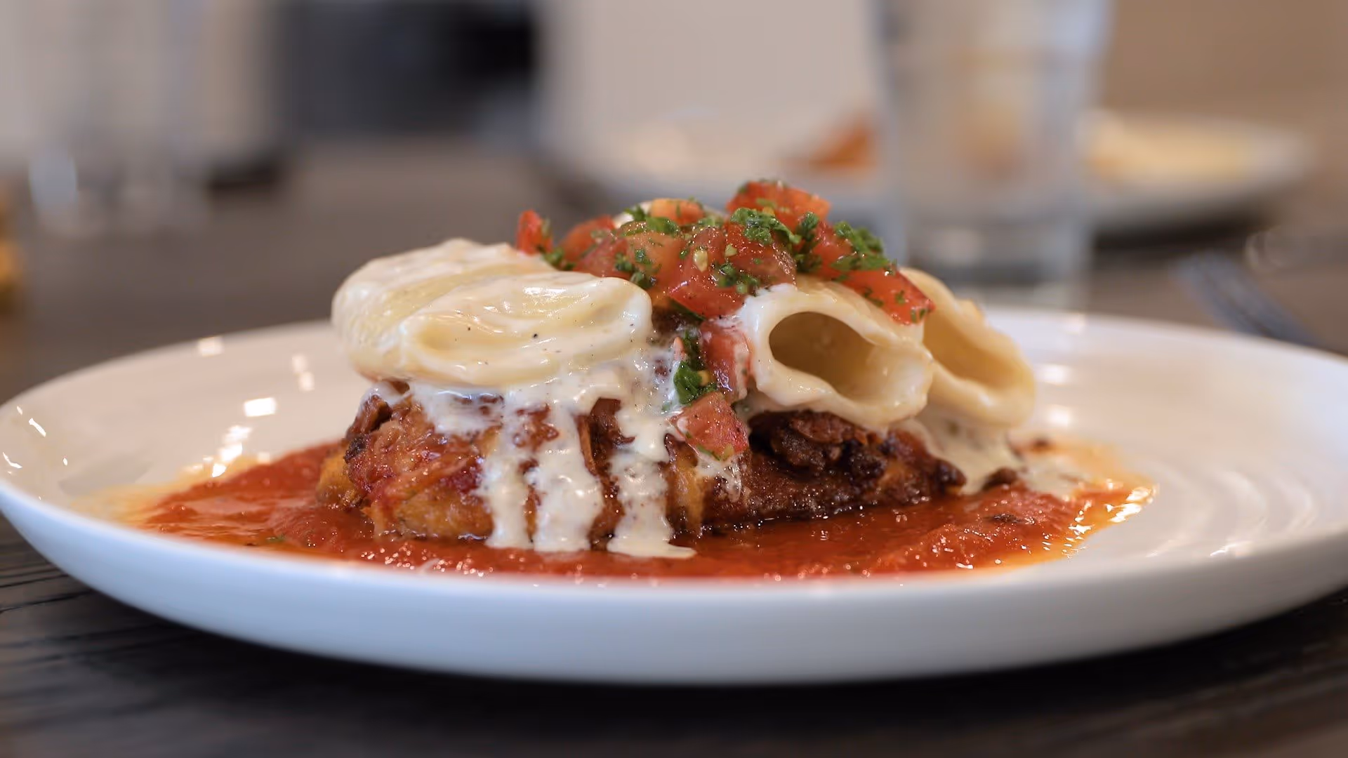 Close-up of a plated pasta dish with large stuffed pasta, tomato sauce, and creamy cheese on a white plate.