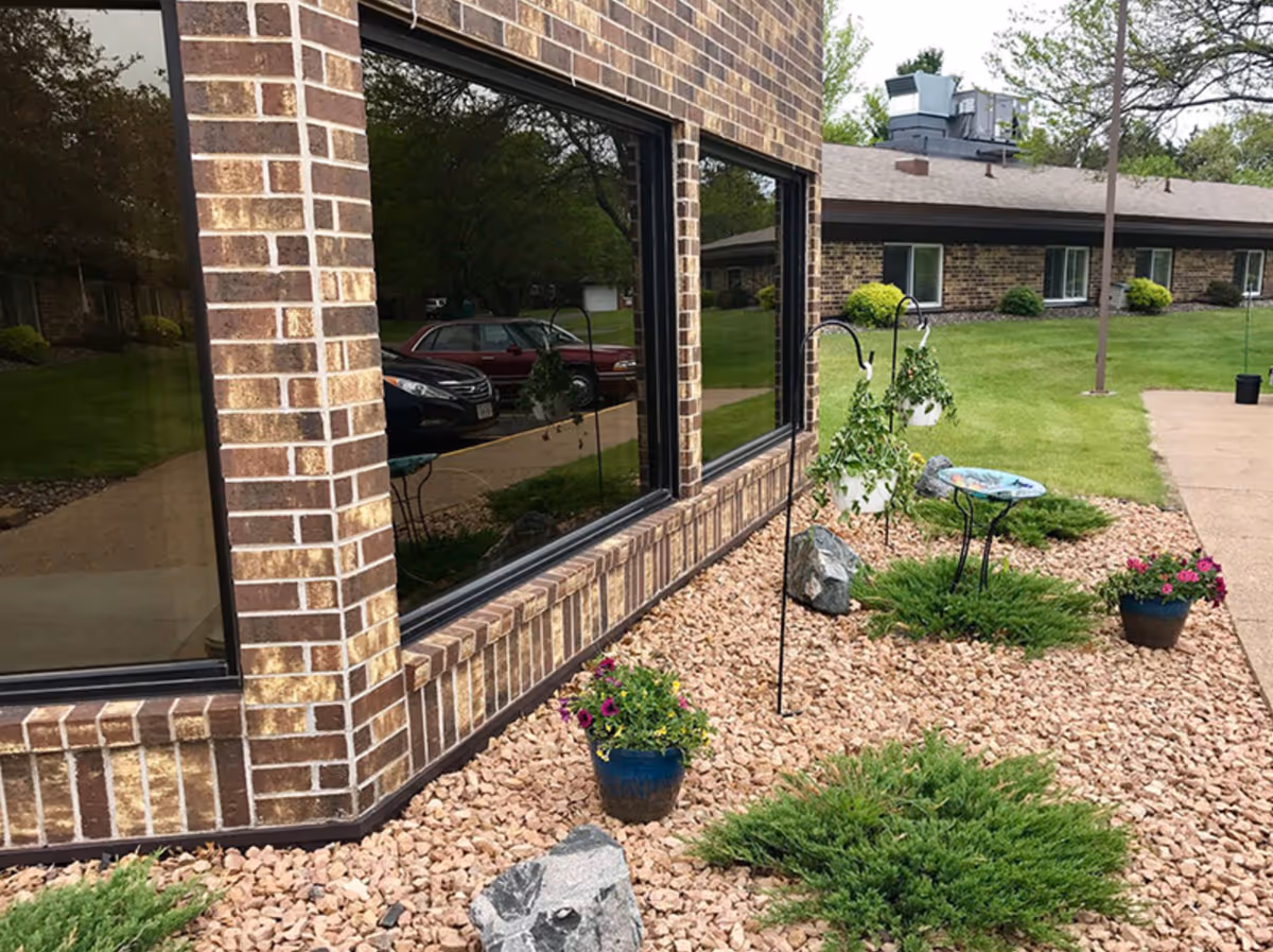 Corner of a brick building with large reflective windows, rock landscaping, potted flowers and a grassy lawn