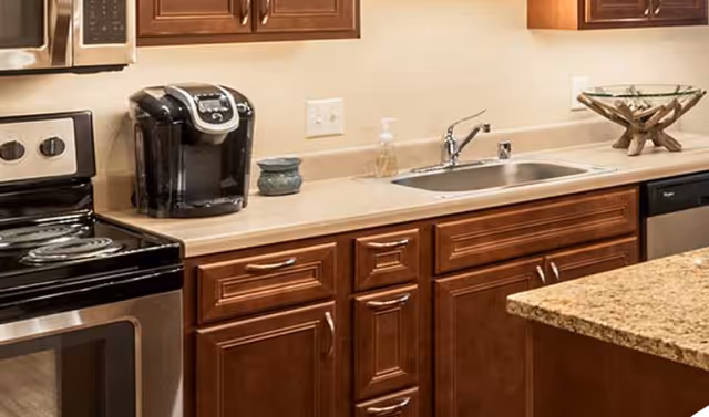 Modern kitchen countertop with stainless steel stove and microwave, a coffee maker, sink, and wooden cabinets.