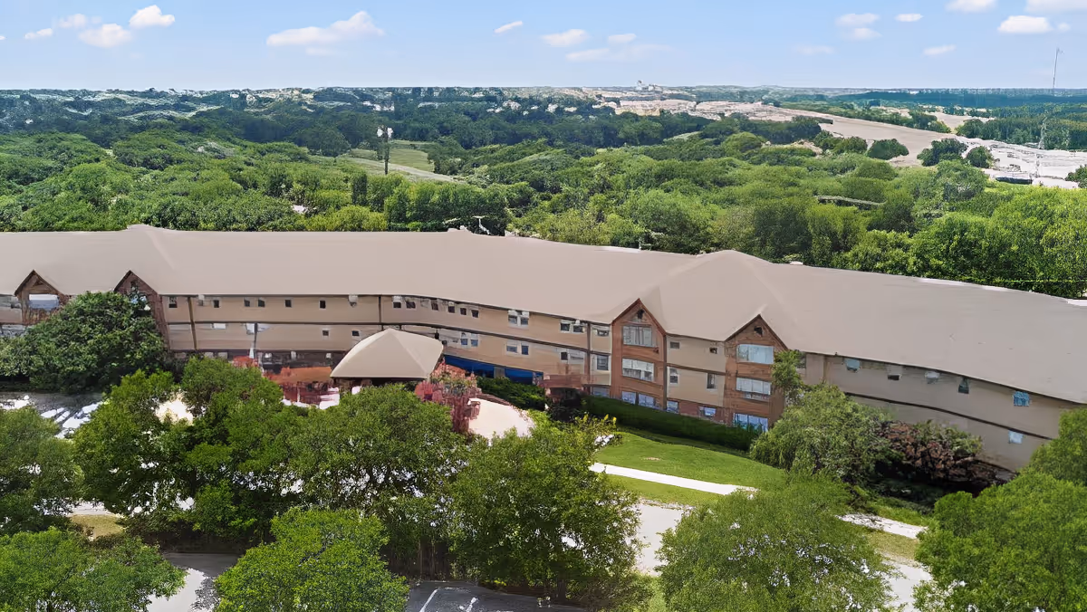 Aerial view of Morada Meadow Lakes facility surrounded by lush green trees and vegetation under a partly cloudy sky.