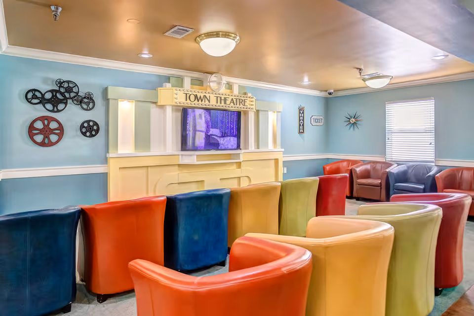 Colorful small theater room with rows of multicolored chairs facing a 'Town Theatre' screen on pastel blue walls.