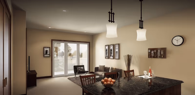 Open-concept living area with a dark granite kitchen island and chairs in the foreground and a sofa with sliding glass doors to a balcony in the background.