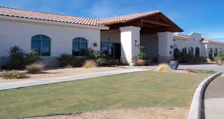 Front exterior of a single-story senior living facility with lawn, shrubs, and planters.