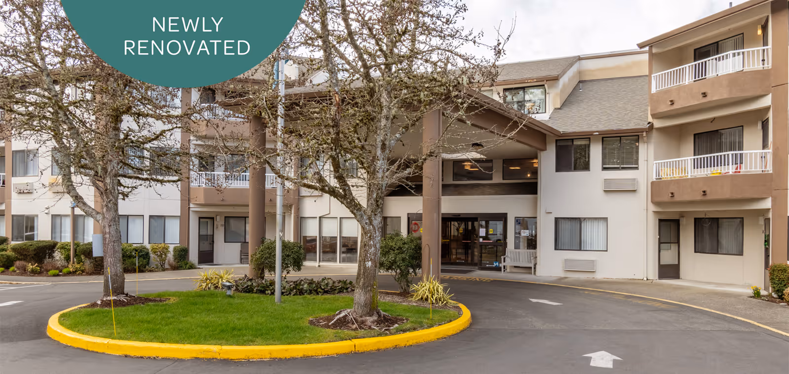Front entrance of a renovated multi-story retirement community building with a circular driveway, landscaped island, and balconies.