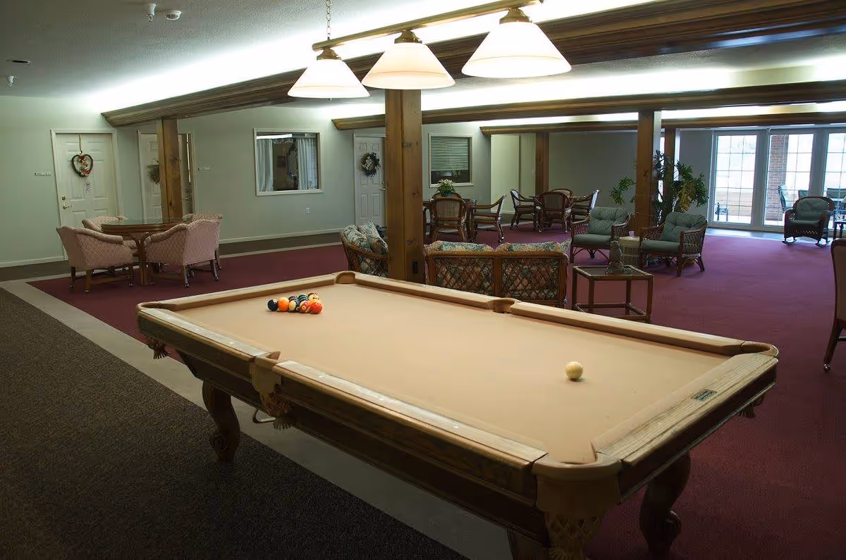 Communal lounge room with a pool table in the foreground and several seating and dining areas in the background.