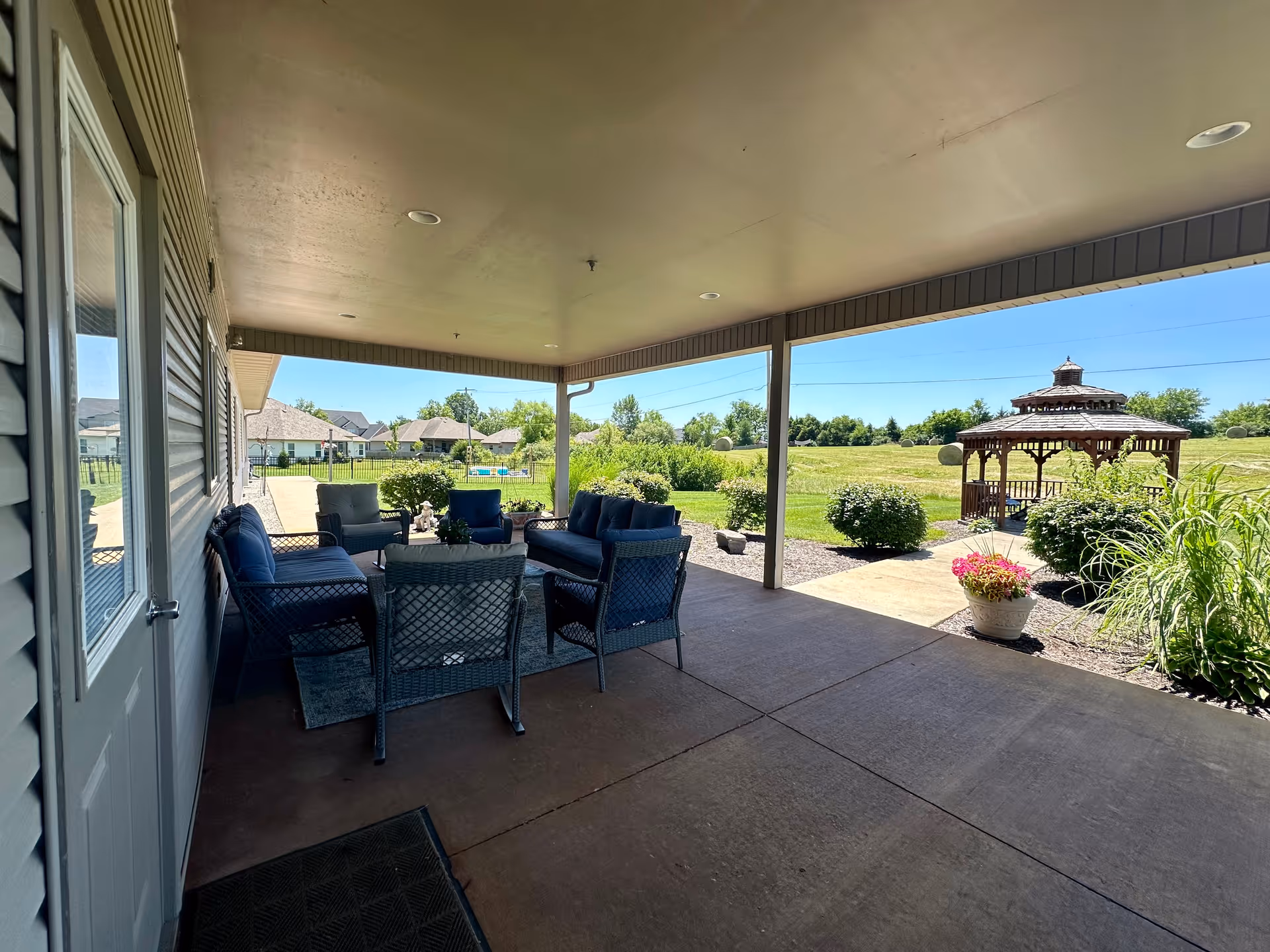 Covered patio with wicker seating overlooking a grassy yard and a wooden gazebo.