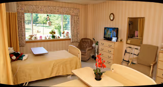 Cozy bedroom in Hathaway Manor Extended Care featuring a bed, dresser, TV, and large window.