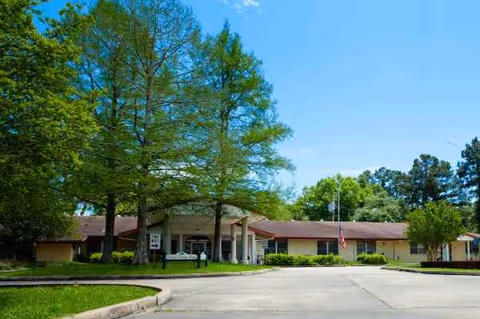 Front exterior of Colonial Nursing Home with trees, driveway, and an American flag near the entrance.