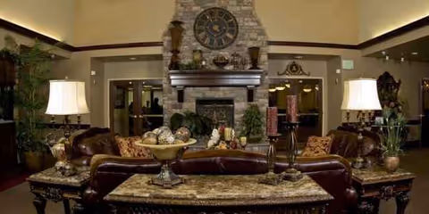 Luxurious indoor lounge in a senior facility with a fireplace, clock mantle, plants, and leather seating.