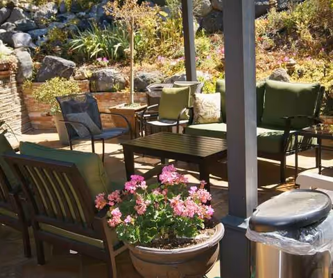 Outdoor seating area with chairs, table, potted pink flowers, and decorative rocks.