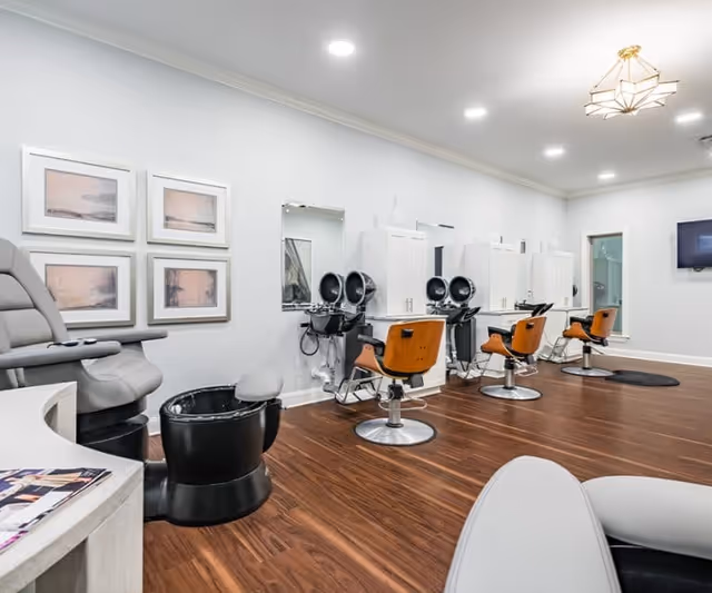 Interior salon with multiple styling chairs, hair-washing stations, and pedicure seating on a wood floor.