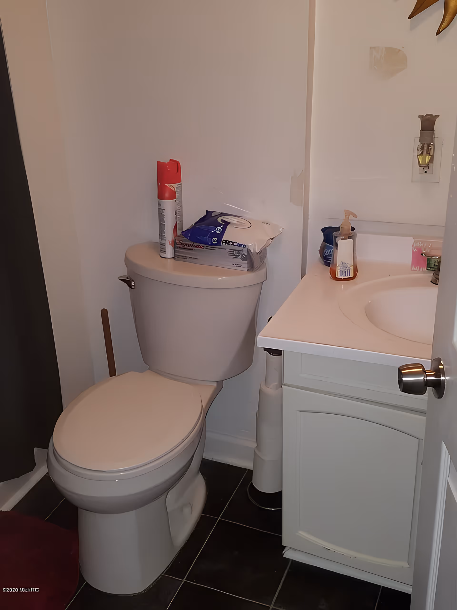 Small bathroom with a toilet next to a vanity sink and toiletries on the tank and counter.