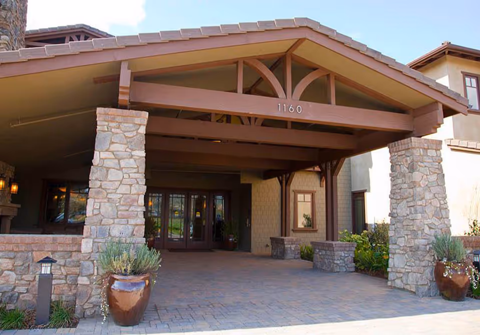 Covered porte-cochere with stone pillars, wooden beams and glass entry doors displaying the address '1160'.