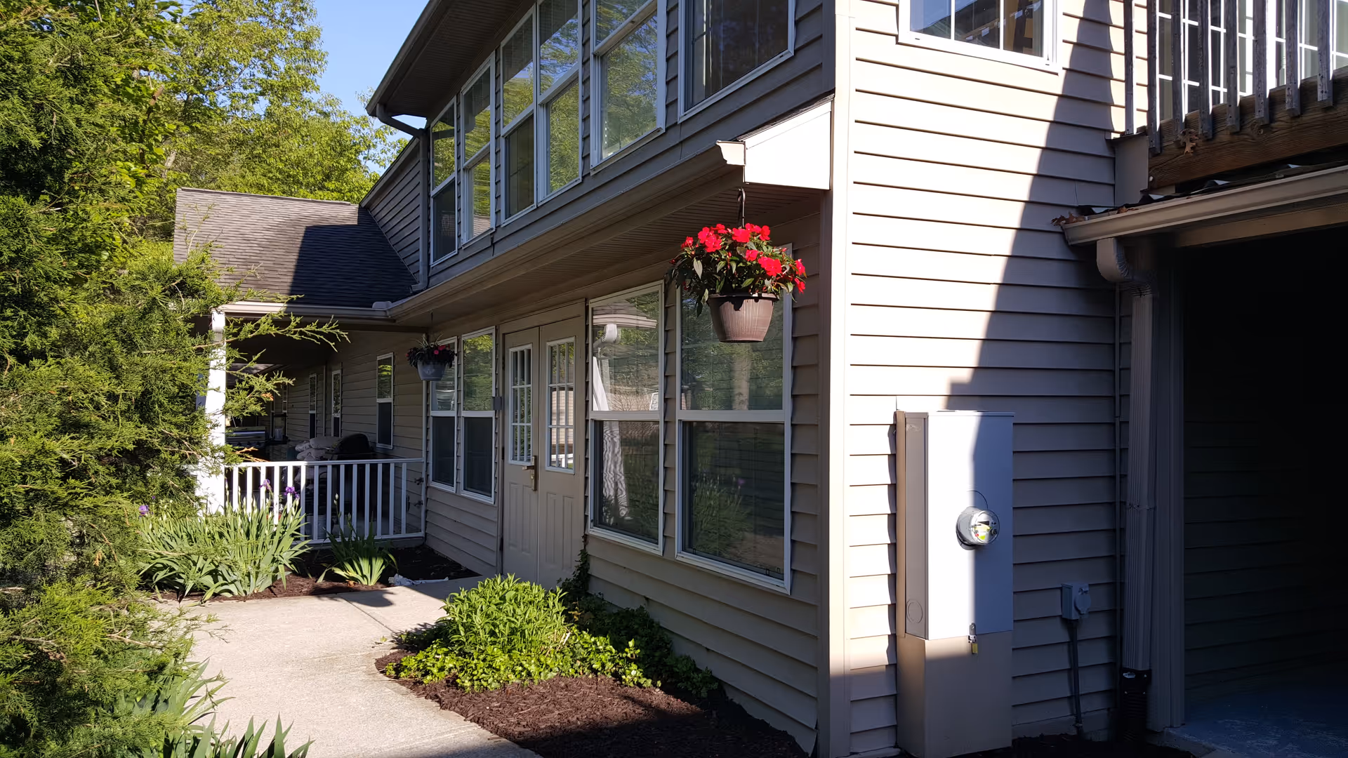 Exterior view of a beige-sided building with a walkway, windows, hanging flower baskets and a small porch.