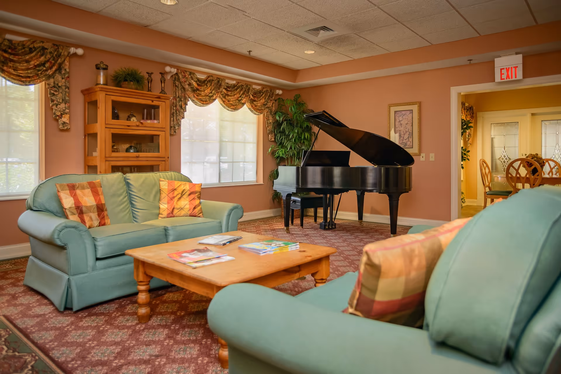 Cozy common living room with green sofas, a wooden coffee table, and a black grand piano against a peach-colored wall.