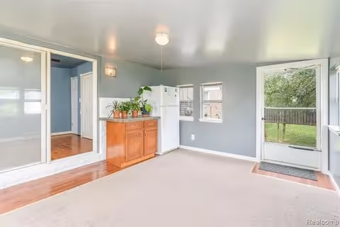 Light-filled interior room with gray walls, a small wooden cabinet topped with potted plants, a refrigerator, mirrored sliding doors, and a screen door leading outside.