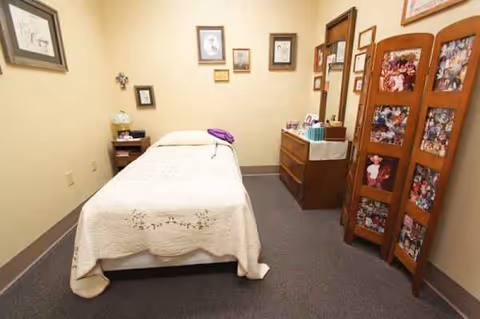 A small, neatly arranged senior living bedroom with a bed, dresser, and photo screen.