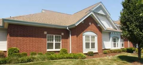 Brick senior living facility front with white-trimmed windows and a manicured lawn.