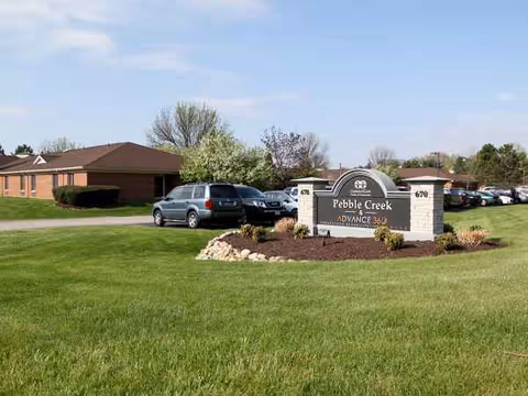 Exterior view of Pebble Creek senior living with a sign and parked cars.