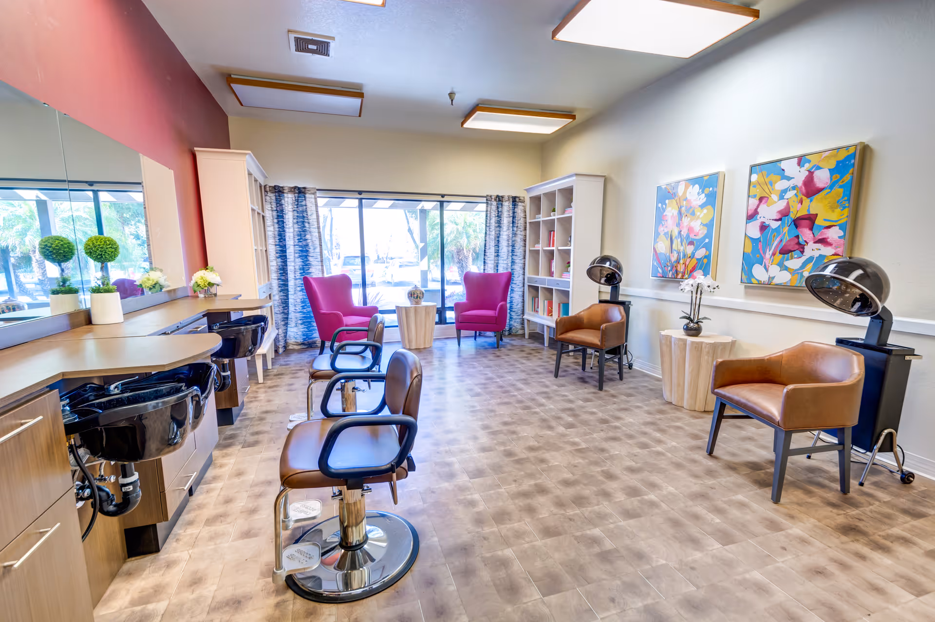 Bright salon-style interior with styling chairs, shampoo sinks, hooded hair dryers and a seating area with colorful artwork.