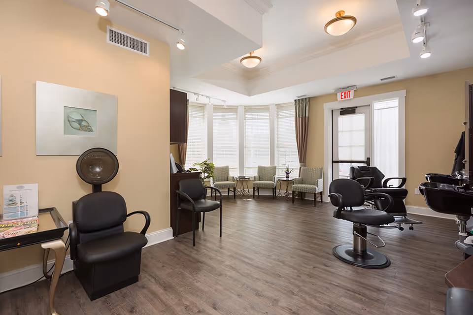 Bright, spacious interior salon with styling chairs, a hooded dryer, washbasins and a seating area by bay windows.