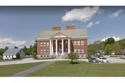 Front exterior of a large brick building with a columned entrance, wide lawn, and a few parked cars.