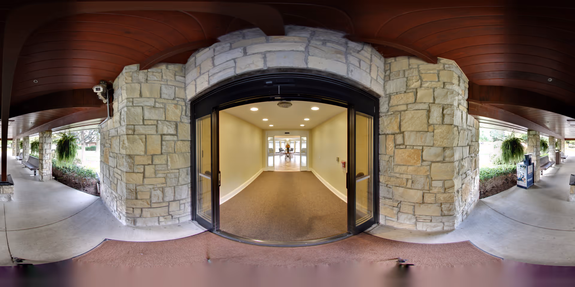 Covered stone entrance with glass double doors leading into a carpeted interior hallway.