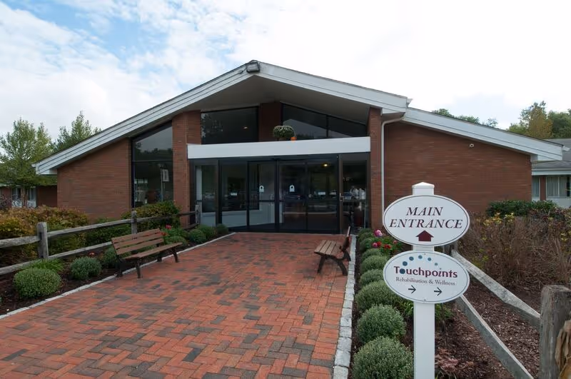 Brick building main entrance with a covered glass door, brick paver walkway, benches, and a 'Main Entrance' sign for Touchpoints.
