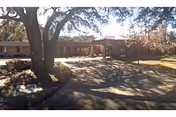 Single-story brick building entrance with a large shade tree and a circular driveway casting shadows.